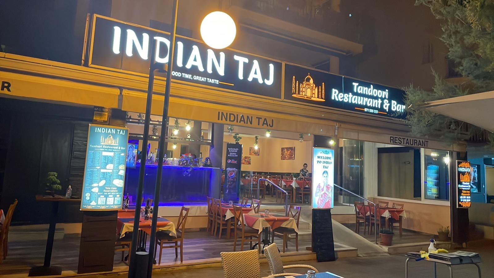 Indian Taj Cala Millor bei Nacht – beleuchtete Fassade des indischen Tandoori-Restaurants am Passeig Marítim mit Terrasse und gedeckten Tischen